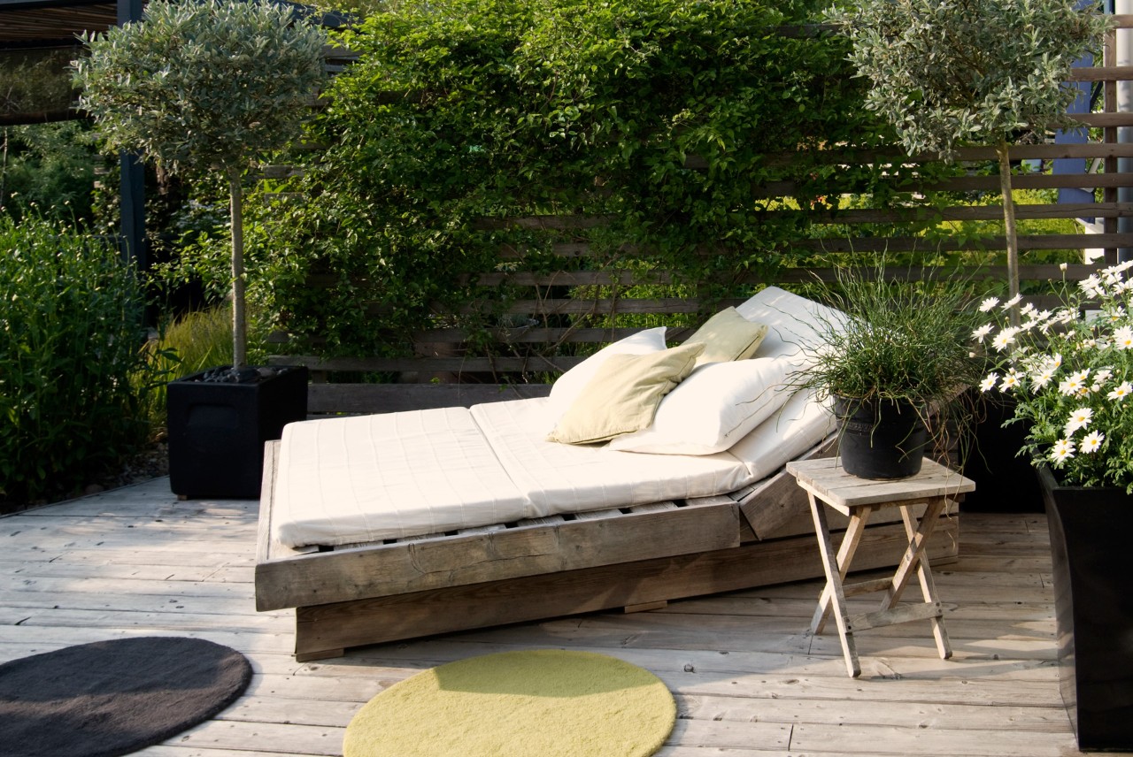 Oase, ontspanningsruimte, ligbank in de kleine tuin, vooraan rond tapijt, rondom plantenbakken, inkijkbescherming.