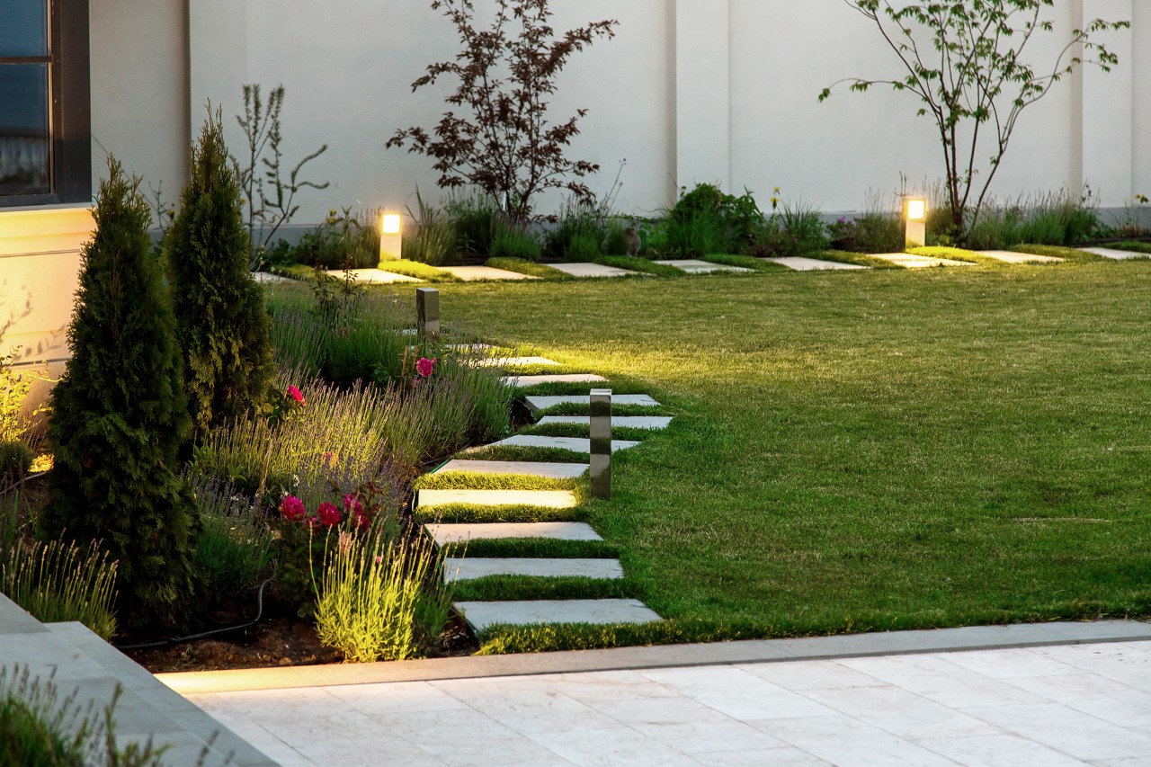 Kleine tuin 's avonds, bloemperk, groen gazon, marmeren vierkante tegels, decoratieve verlichting op de grond.