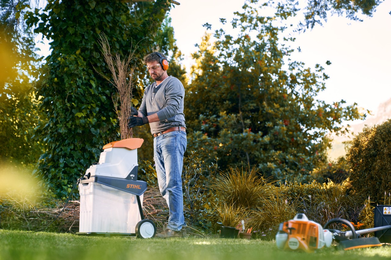 Man met gehoorbescherming versnippert takjes om te composteren met een STIHL elektrische hakselaar GHE 140