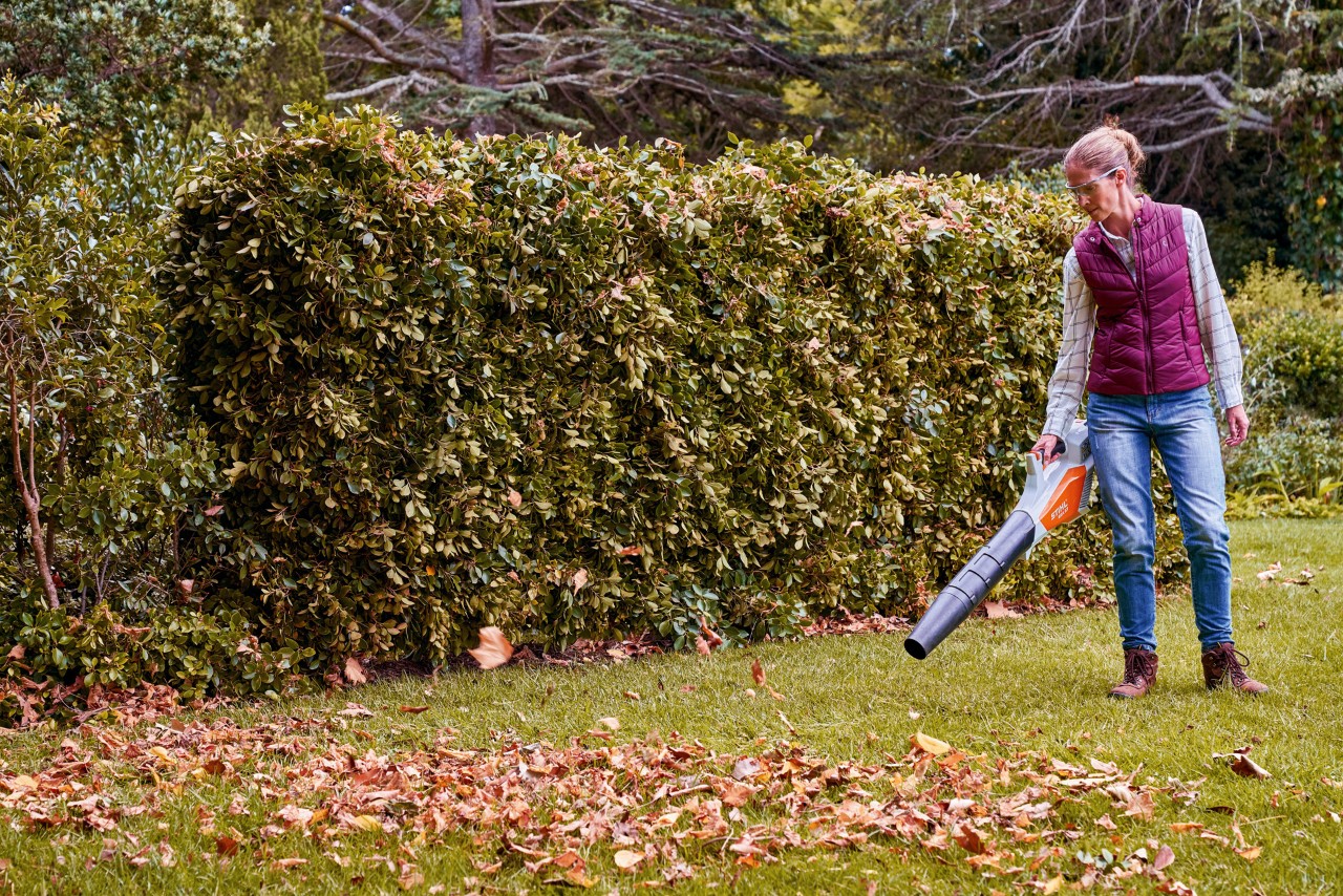 Een vrouw blaast bladeren op een gazon bij elkaar met een STIHL BGA 57 accubladblazer