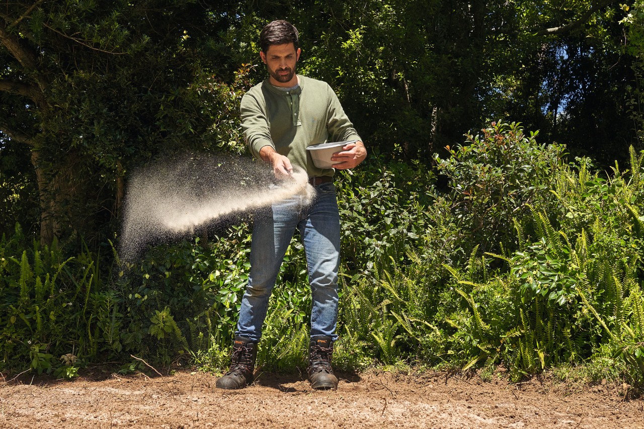 Een man strooit zaad uit voor een wilde bloemenweide  