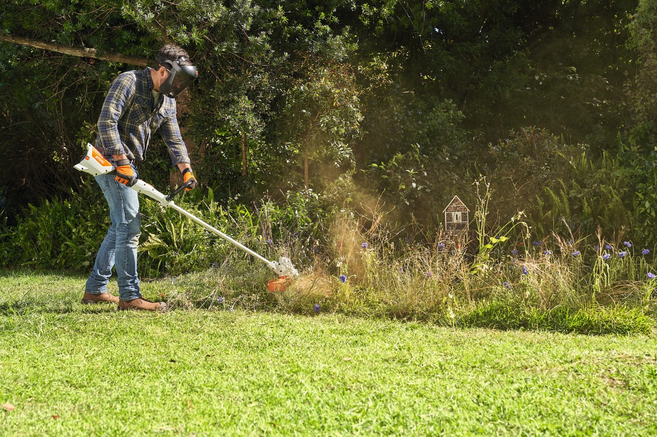 Een man in veiligheidsuitrusting maait met de STIHL FSA 57 accukantenmaaier een weide met wilde bloemen  